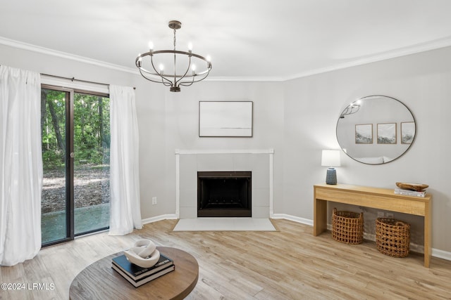 living room featuring a tiled fireplace, ornamental molding, hardwood / wood-style flooring, and an inviting chandelier