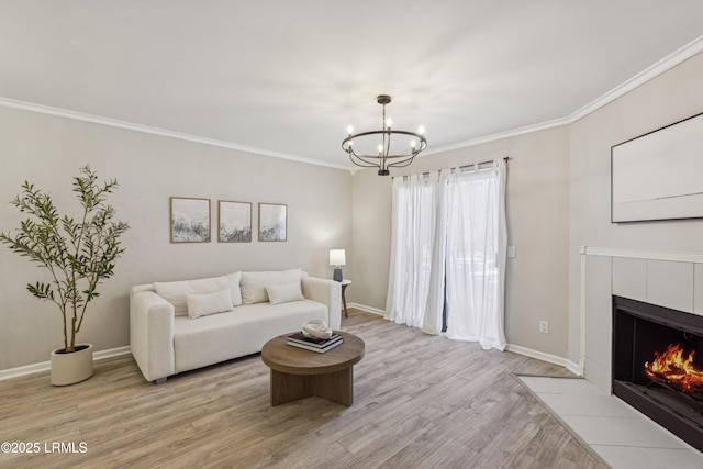 living room featuring a tiled fireplace, crown molding, light hardwood / wood-style flooring, and an inviting chandelier