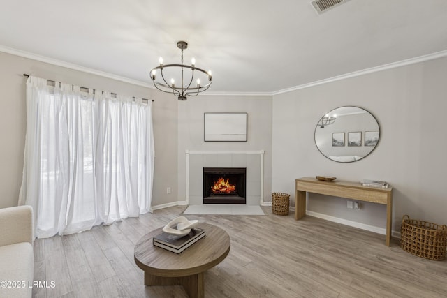 living room featuring a notable chandelier, hardwood / wood-style flooring, ornamental molding, and a tile fireplace