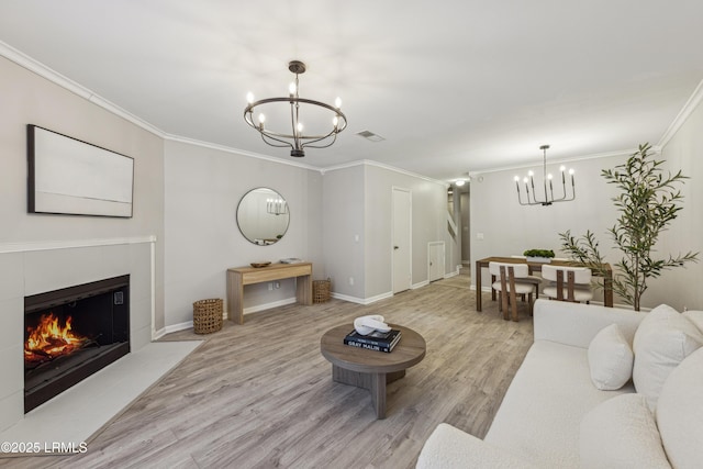 living room featuring a tiled fireplace, ornamental molding, a chandelier, and light wood-type flooring