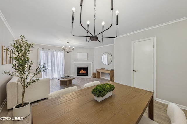 dining area featuring a tile fireplace, a notable chandelier, crown molding, and light hardwood / wood-style flooring