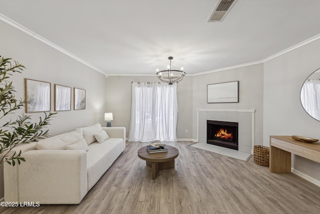 living room featuring crown molding, a chandelier, a fireplace, and light wood-type flooring