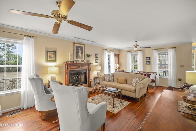 living room featuring a healthy amount of sunlight, visible vents, a fireplace, crown molding, and light wood-type flooring