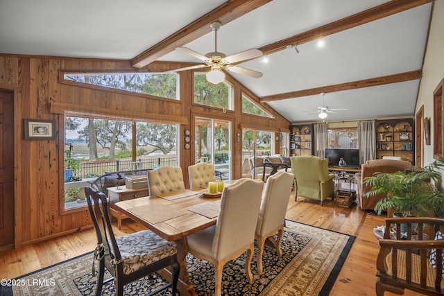 dining room featuring beam ceiling, wood walls, a ceiling fan, and light wood-style floors