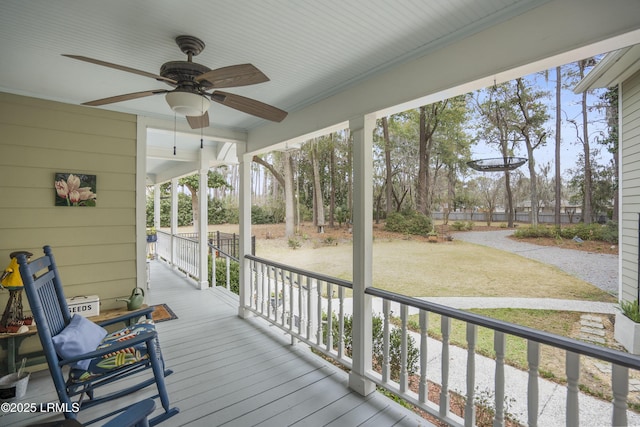 wooden terrace with covered porch, a lawn, and a ceiling fan