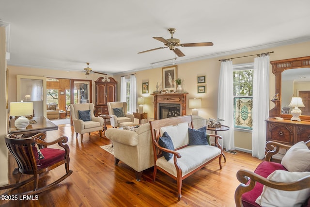 living area with ornamental molding, a fireplace, a ceiling fan, and wood finished floors