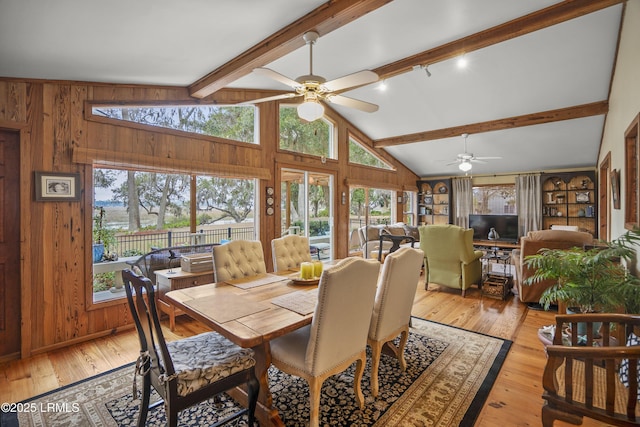 dining room featuring wood walls, a ceiling fan, vaulted ceiling with beams, and light wood-style flooring