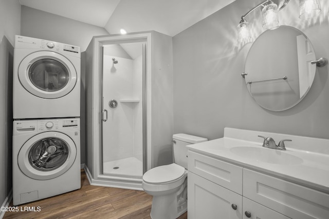 full bath featuring vanity, wood finished floors, a shower stall, stacked washer and dryer, and toilet