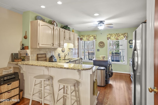 kitchen featuring dark wood finished floors, decorative backsplash, a peninsula, freestanding refrigerator, and a sink