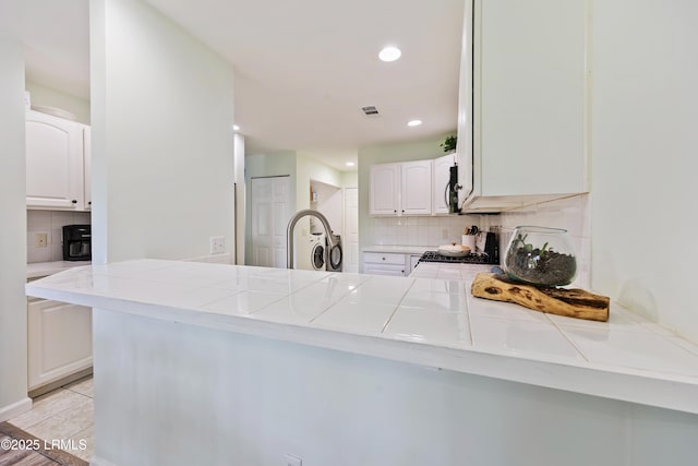 52 Lake Linden Ln Unit 52, Bluffton, SC 29910 - kitchen with stove, tasteful backsplash, white cabinets, tile countertops, and a peninsula