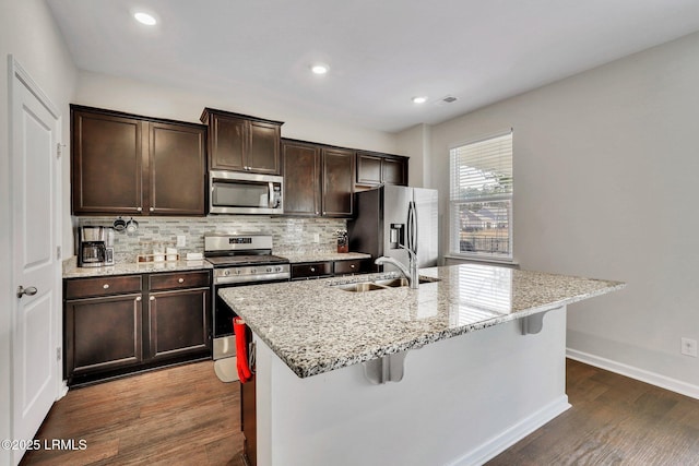 kitchen with stainless steel appliances, dark wood-type flooring, a center island with sink, and a kitchen bar