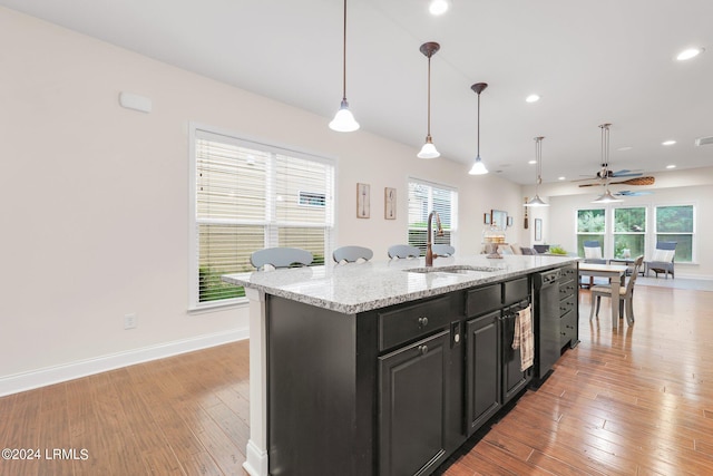 kitchen featuring sink, hanging light fixtures, a kitchen island with sink, stainless steel dishwasher, and light stone countertops