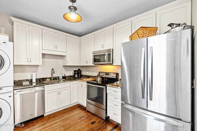 kitchen with white cabinetry, appliances with stainless steel finishes, dark stone counters, stacked washing maching and dryer, and hardwood / wood-style floors