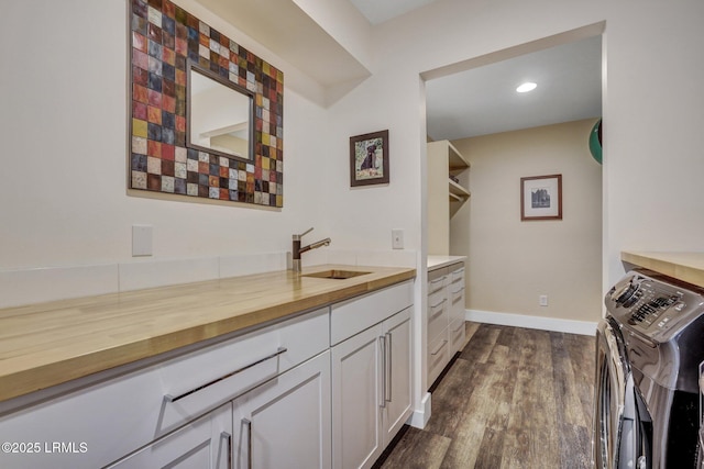 bar featuring dark wood-type flooring, butcher block countertops, sink, washing machine and dryer, and white cabinets