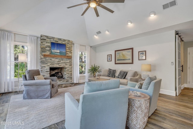 living room with hardwood / wood-style flooring, a stone fireplace, high vaulted ceiling, and ceiling fan