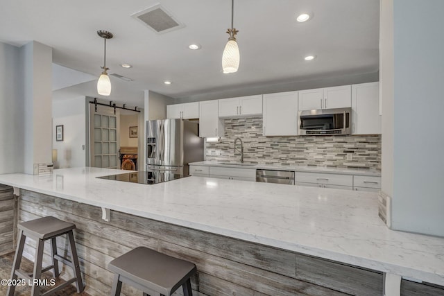 kitchen featuring a breakfast bar, a barn door, white cabinets, and appliances with stainless steel finishes