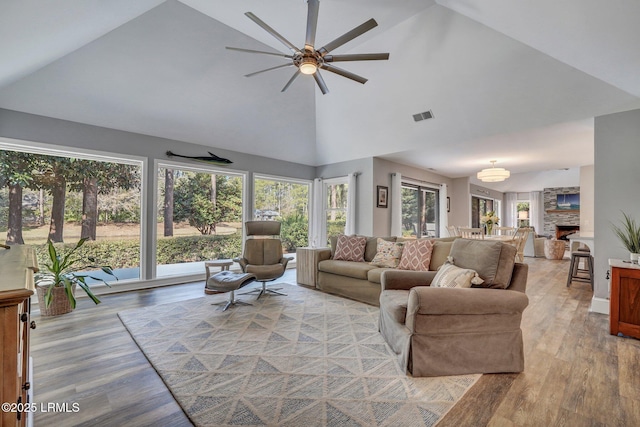 living room with a stone fireplace, high vaulted ceiling, and light hardwood / wood-style flooring