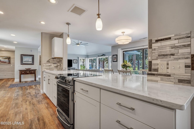 kitchen featuring stainless steel range with electric stovetop, light stone countertops, white cabinets, decorative light fixtures, and kitchen peninsula