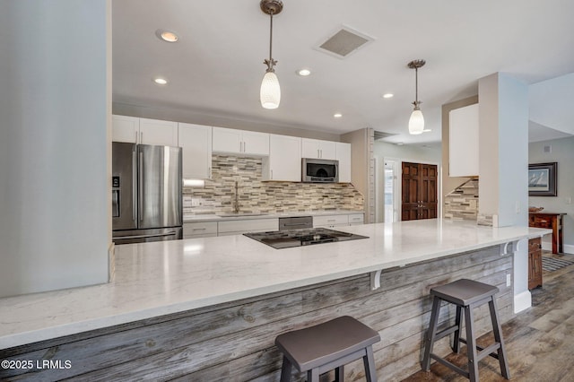 kitchen featuring light stone counters, appliances with stainless steel finishes, kitchen peninsula, pendant lighting, and white cabinets