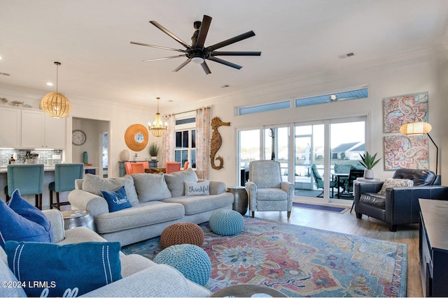 living room with ornamental molding, ceiling fan with notable chandelier, and light wood-type flooring