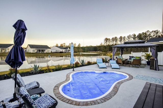 pool at dusk with a gazebo, a patio, and a water view