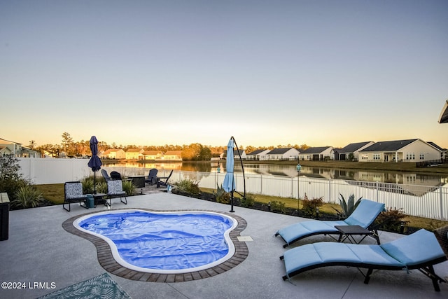 pool at dusk with a water view and a patio area