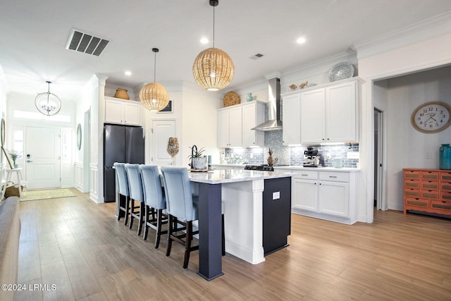 kitchen featuring pendant lighting, white cabinetry, backsplash, a kitchen island with sink, and wall chimney exhaust hood