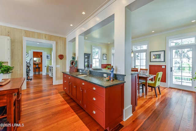 kitchen with dark stone countertops, crown molding, light wood-style floors, and a sink