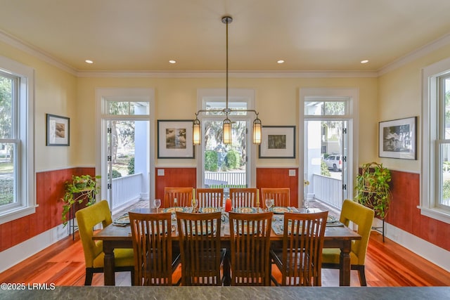 dining space featuring wood finished floors, crown molding, a healthy amount of sunlight, and wainscoting