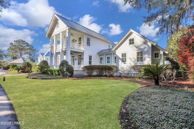 view of front of house with a balcony, a ceiling fan, a standing seam roof, a front lawn, and metal roof