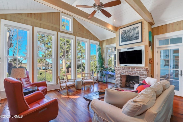 living room with wooden walls, a brick fireplace, vaulted ceiling with beams, ceiling fan, and hardwood / wood-style floors