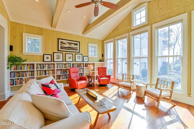 living area with beam ceiling, wood finished floors, wood walls, and ceiling fan