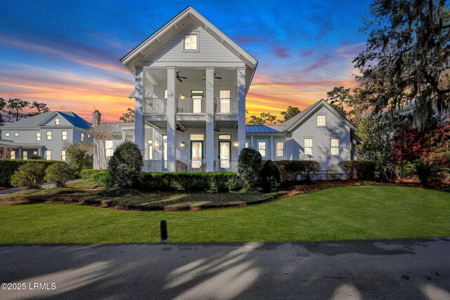 greek revival house with a ceiling fan, a standing seam roof, a yard, metal roof, and a balcony