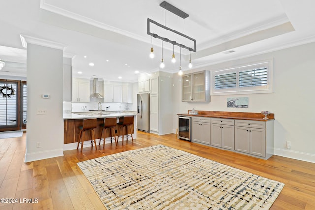 kitchen with beverage cooler, crown molding, a raised ceiling, stainless steel refrigerator with ice dispenser, and wall chimney range hood