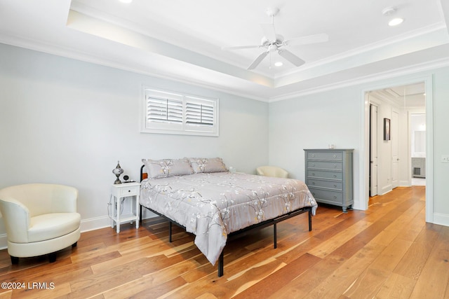 bedroom with ornamental molding, light hardwood / wood-style flooring, ceiling fan, and a tray ceiling