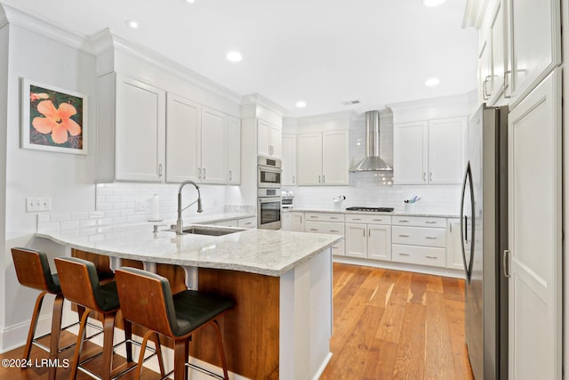 kitchen with wall chimney range hood, sink, stainless steel refrigerator, light stone counters, and white cabinets