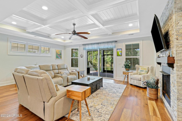 living room featuring coffered ceiling, a stone fireplace, beam ceiling, and light wood-type flooring