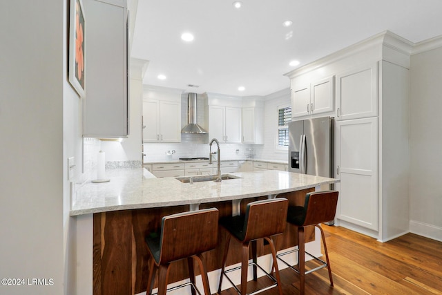 kitchen featuring white cabinetry, sink, a kitchen breakfast bar, wall chimney range hood, and light wood-type flooring