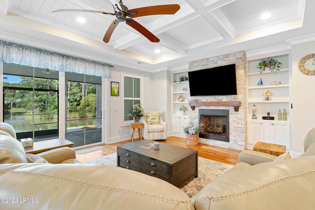 living room with ornamental molding, a stone fireplace, coffered ceiling, and light wood-type flooring