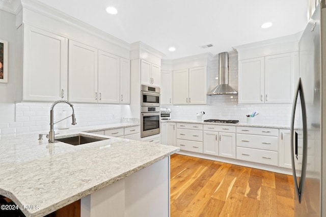 kitchen featuring sink, white cabinets, stainless steel appliances, light stone countertops, and wall chimney range hood