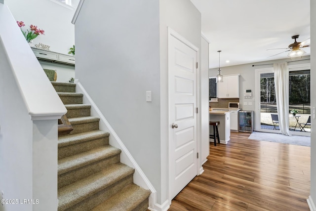 stairway featuring ceiling fan, wine cooler, baseboards, and wood finished floors