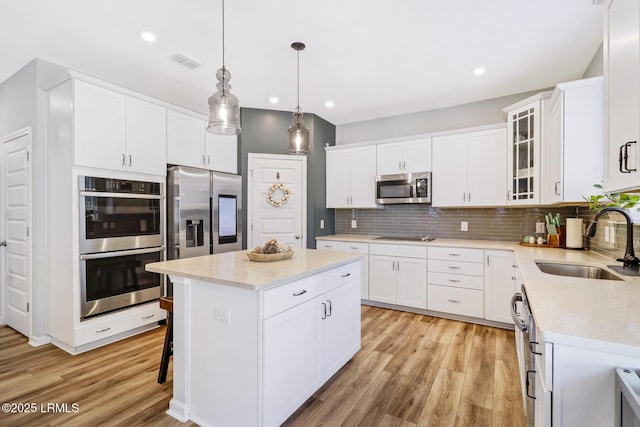 kitchen with tasteful backsplash, white cabinets, a kitchen island, appliances with stainless steel finishes, and a sink