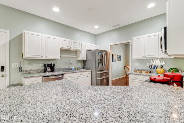 kitchen featuring stainless steel appliances, white cabinetry, sink, and light stone counters