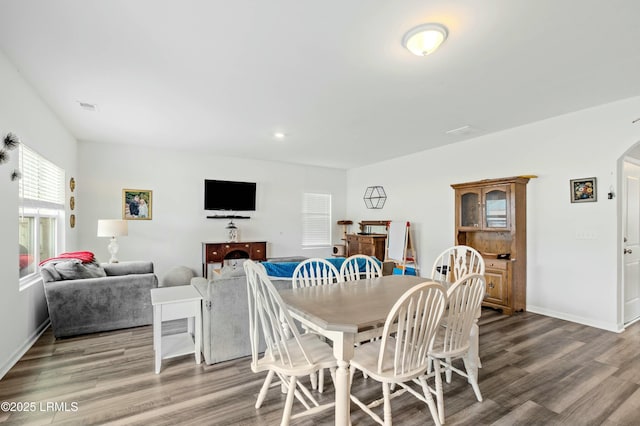 dining area with baseboards, visible vents, arched walkways, and wood finished floors