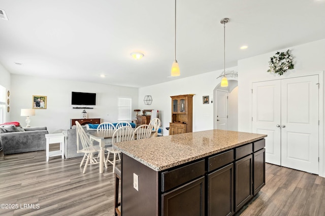 kitchen with arched walkways, open floor plan, decorative light fixtures, dark brown cabinets, and light wood-type flooring