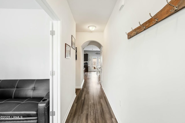 hall featuring arched walkways, dark wood-style floors, and baseboards