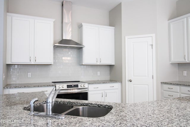 kitchen with wall chimney range hood, stainless steel range with electric stovetop, white cabinets, and a sink