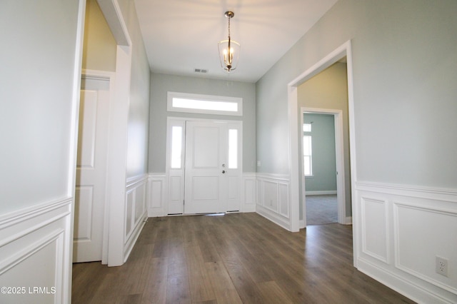 foyer entrance featuring dark wood finished floors, wainscoting, visible vents, and plenty of natural light