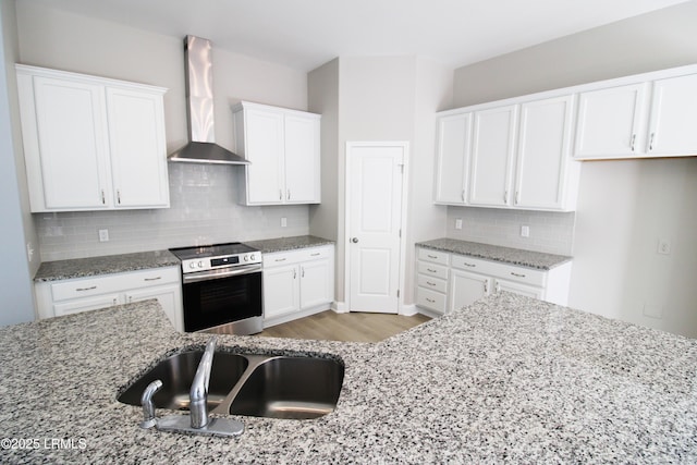 kitchen with stainless steel range with electric stovetop, wall chimney exhaust hood, light stone counters, and a sink