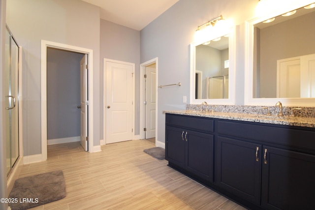 full bath with double vanity, baseboards, wood tiled floor, a shower stall, and a sink